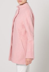 Abrigo de fieltro rosa con cuello alto, bolsillos laterales y silueta recta. Textura suave, diseño minimalista y sin herrajes prominentes.
