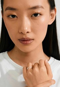 Anello d'argento con un design delicato indossato su una mano. La persona ha la pelle liscia, i capelli scuri e indossa una maglietta bianca. Ritratto ravvicinato.