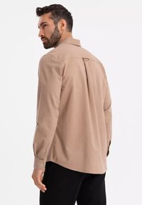 Chemise beige à boutons, avec un pli dans le dos, manches longues et poignets à boutons. Texture unie avec un léger éclat. Coupe cintrée.