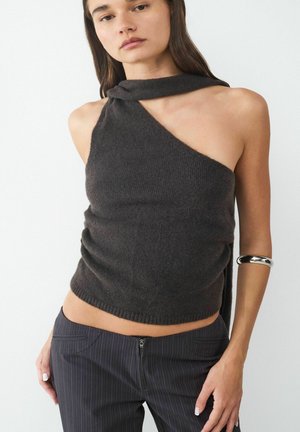 Haut en tricot marron foncé ajusté avec un design asymétrique unique et un col torsadé. Associé à un pantalon à rayures fines bien coupé et un bracelet en argent.