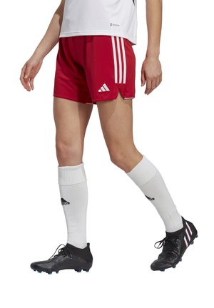 Red sports shorts with three white stripes, paired with black soccer cleats and white knee-high socks. The outfit is performance-oriented.