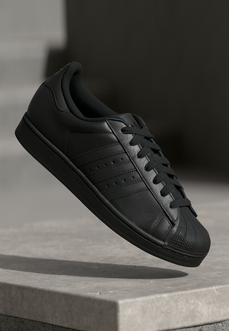 Baskets en cuir noir avec un capuchon texturé, des lacets plats et trois bandes sur le côté. Surface lisse et forme arrondie.