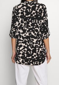 Svart och beige abstrakt djurtryck skjortblus med trekvartslånga ärmar och rundad nederkant, tillverkad av lättviktsmaterial.