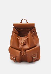 Mochila de cuero marrón con forma redondeada, cierre de cordón y dos bolsillos con solapa magnética. Cuenta con una asa superior para facilitar su transporte.