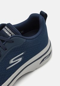 Scarpa sportiva blu navy con tomaia in rete testurizzata, dettagli bianchi e suola ammortizzata etichettata "ArchFit". Presenta lacci scuri e un design a profilo basso.