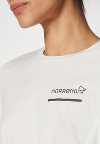 Fehér technikai póló, fekete "NORRØNA" logóval. Simább textúra, kerek nyakkivágás, rövid ujjú, sportoláshoz tervezve.