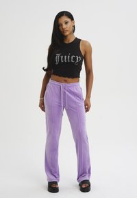 Top corto nero con design "Juicy", abbinato a pantaloni in velluto viola chiaro con strisce laterali e cintura elastica. Sandali neri con zeppa.