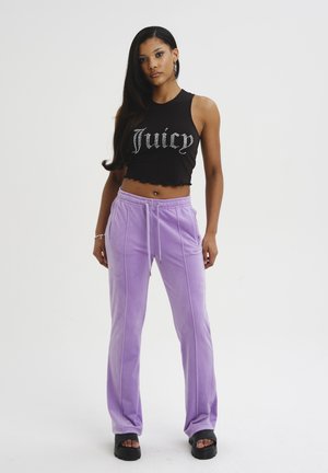 Top corto nero con design "Juicy", abbinato a pantaloni in velluto viola chiaro con strisce laterali e cintura elastica. Sandali neri con zeppa.
