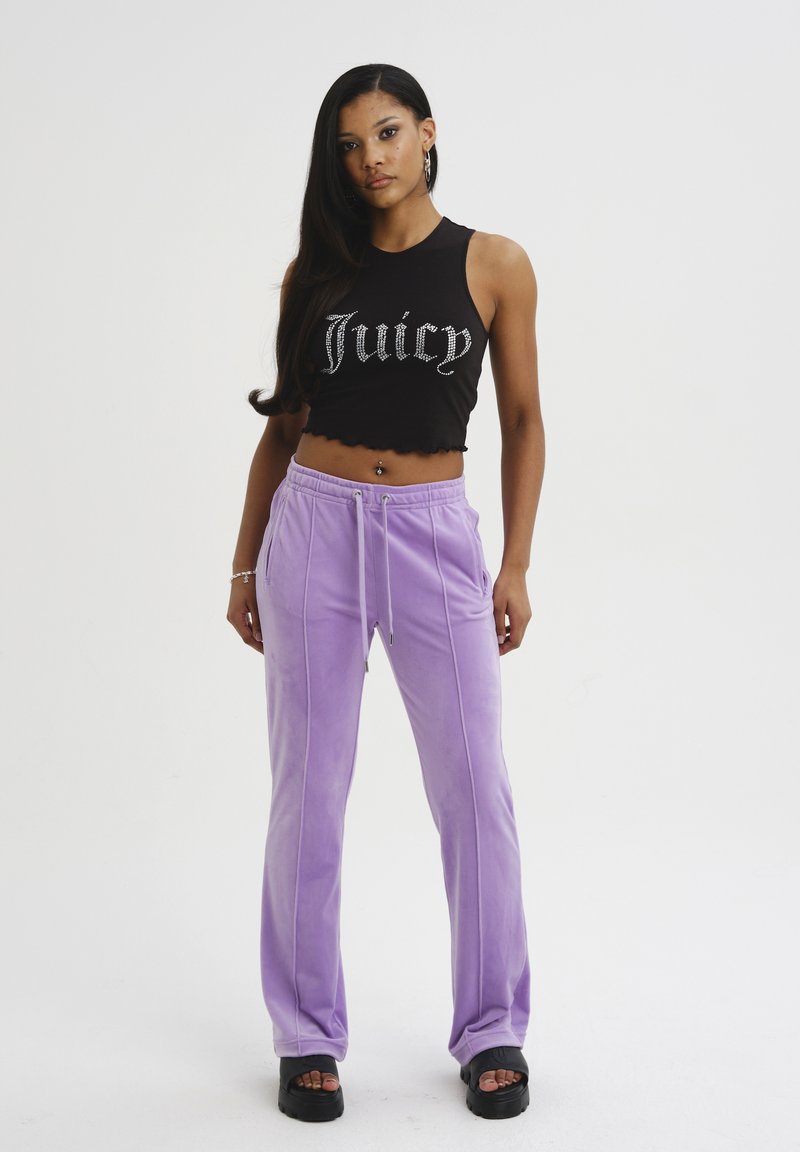 Top corto nero con design "Juicy", abbinato a pantaloni in velluto viola chiaro con strisce laterali e cintura elastica. Sandali neri con zeppa.