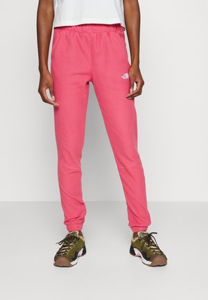 Personne portant un pantalon de survêtement rose vif avec une taille élastique et des chaussures de sport vert olive, noir et marron.