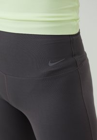 Crne tajice s glatkim, rastezljivim materijalom i suptilnim Nike logotipom na struku. Uparene s svijetlozelenom tijesnom majicom.