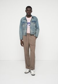 Gaiši zila džinsa jaka, rozā grafiska T-krekls, bēšas sporta bikses ar sānu svītrām un baltas sporta kurpes ar melniem akcentiem.