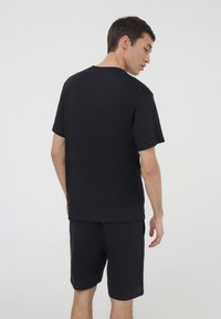 T-shirt in cotone nero con vestibilità rilassata, maniche corte e scollo rotondo, abbinata a pantaloni corti neri coordinati in un design semplice.