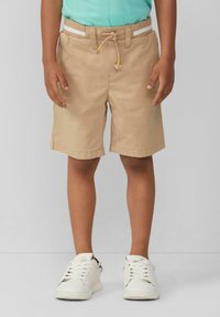 Shorts en coton beige avec une taille réglable dotée d'un cordon de serrage et de légères rayures. Associés à des baskets blanches.