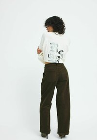 Sweatshirt in cream with a large graphic print in shades of grey on the back, paired with dark brown corduroy pants featuring back pockets.