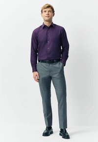 Fioletowa koszula z długim rękawem, połączona z jasnoszarymi spodniami w kratkę i czarnymi butami. Koszula ma klasyczny kołnierzyk i zapięcie na guziki.