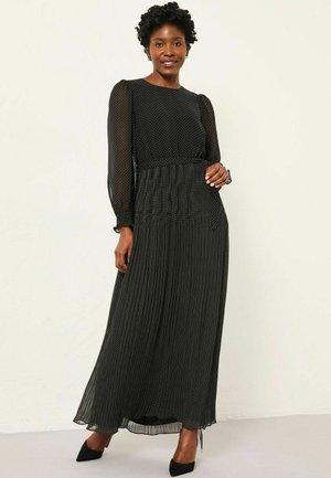 Black long-sleeve dress featuring a polka dot pattern, pleated skirt, sheer fabric, and fitted waist. Paired with black high-heeled shoes.