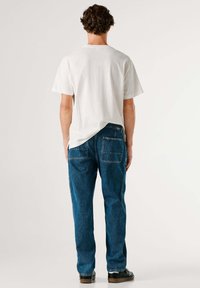 Valge puuvillane lühikeste varrukatega T-särk, tagant vaates; kombineeritud siniste denimist teksapükstega, millel on kaks tagataskut ja sirge lõige.