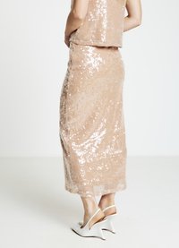 Beige Pailletten-Zweiteiler mit einem kurz geschnittenen Oberteil und einem figurbetonten Rock. Verfügt über eine gerippte Struktur und einen dezenten Glanz. Kombiniert mit weißen Absatzschuhen.