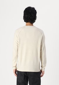 Pull long à manches longues beige clair avec un motif tricoté texturé et des rayures alternées, col rond et poignets côtelés.