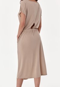Béžové šaty s krátkými rukávy, elastickým pasem, sukní střední délky a detailem v podobě klíčové díry na zádech. Vyrobeno ze měkké, hladké látky.