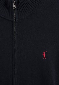 Maglione blu navy scuro con zip in maglia, colletto a coste e piccolo logo ricamato a rosso di un giocatore di polo sul petto.