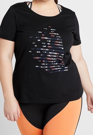 Frau trägt ein schwarzes Kurzarmshirt mit einem fragmentierten runden Grafikmotiv und orange-schwarze Leggings.