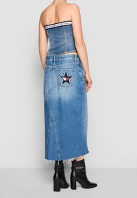 Top sin tirantes de mezclilla con una banda de marca, combinado con una falda de mezclilla de talle alto que presenta un parche de estrella en la parte posterior y un dobladillo deshilachado. Botas de tacón negras.