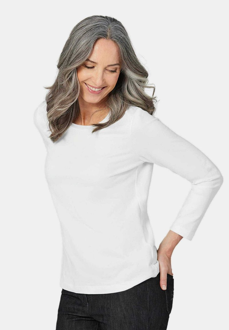 Weißes Langarmhemd mit rundem Ausschnitt, glatter Textur und figurbetontem Design, kombiniert mit dunklen Jeans.