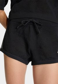 Čierne pletené šortky s textúrovaným vzorom, elastickým pásom a šnúrkou na stiahnutie. Lem má pevný čierny lem.
