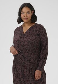 Chemise à manches longues à imprimé floral sombre, avec un col en V et un ourlet froncé. Fabriquée en tissu doux avec une coupe ample et décontractée.