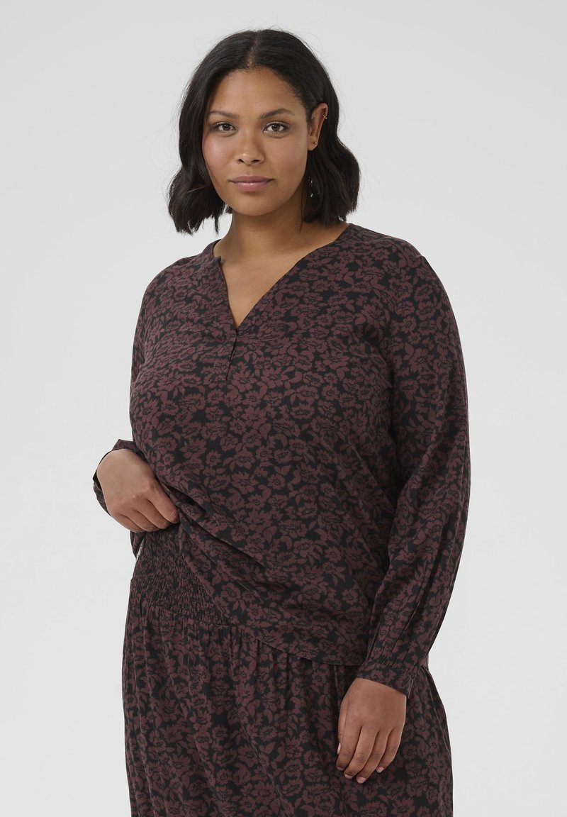 Chemise à manches longues à imprimé floral sombre, avec un col en V et un ourlet froncé. Fabriquée en tissu doux avec une coupe ample et décontractée.