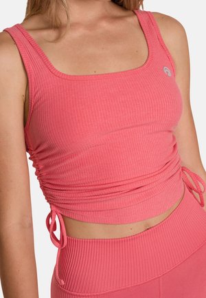 Femme portant un crop top rose côtelé sans manches avec des liens latéraux réglables et des leggings taille haute assortis.