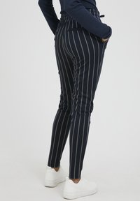 Námořnické pruhované kalhoty se slim fit, s bílými pruhy, elastickým pasem a bočními kapsami, spárované s bílými teniskami.