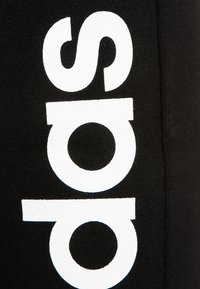 Zwarte kledingstuk met grote witte tekst in een afgerond lettertype. De textuur lijkt zacht en gebreid, wat een casual ontwerp benadrukt.