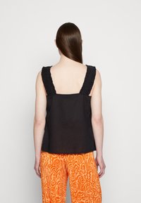 Top preto sem mangas com alças franzidas, feito de um tecido leve, combinado com calças laranja brilhante com padrão abstrato.