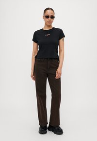 Zwarte T-shirt met korte mouwen met "Ciao Bella" geborduurd in het rood, gecombineerd met donkere bruin hoge taille broeken en zwarte chunky schoenen.