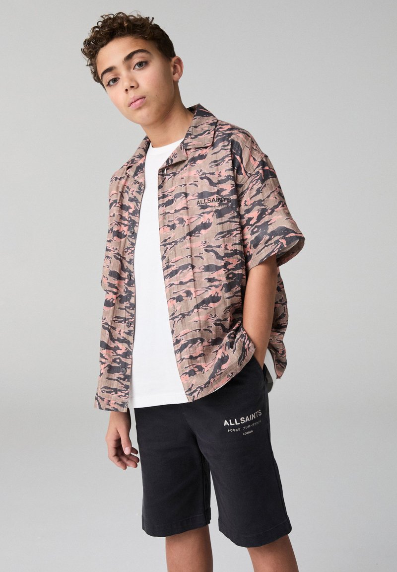 Krátka košeľa na zapínanie na gombíky s ružovo-čiernym maskáčovým vzorom, skombinovaná s čiernymi šortkami. Textové logo na košeli a šortkách.