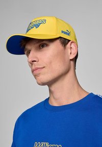 Żółta czapka z niebieskimi akcentami, z logo "Williams Racing"; wykonana z mieszanki bawełny; w zestawie z niebieską koszulką również z detalem logo.