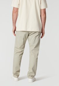 Lichtbeige katoenen t-shirt in combinatie met lichtgrijze chinos en witte sneakers, van achter bekeken, waarbij de pasvorm en materialen van de kleding worden benadrukt.