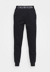 Czarne spodnie dresowe Calvin Klein z elastycznym paskiem w talii, z białym logo Calvin Klein, zwężanymi nogawkami i ściągaczami na kostkach.