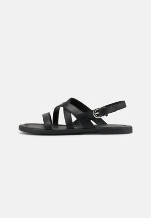 Zwarte platte sandaal met drie leren banden over de voet en verstelbare gespsluiting rond de enkel, zijaanzicht op witte achtergrond.