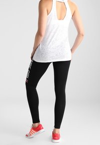 Biały, teksturowany top na ramiączkach typu racerback zestawiony z czarnymi legginsami z białym napisem po bokach; czerwone tenisówki z białymi paskami.