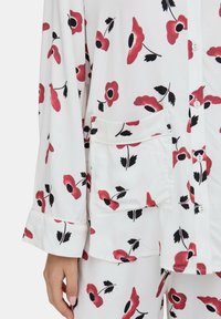 Weißes Pyjama-Set mit rotem Mohnblumenmuster und schwarzen Akzenten. Weicher Stoff, durchgeknöpft vorne und mit einer aufgesetzten Tasche am Oberteil.