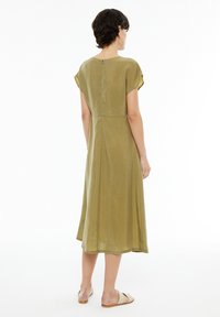 Olivgrünes Midikleid mit kurzen Capärmelchen, Knopfverschluss hinten und einer glatten Textur, die bis knapp unter die Knie reicht.