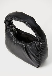 Sac à main noir en tissu matelassé. Il dispose d'une poignée courte et d'une fermeture éclair. Texture lisse avec une forme triangulaire structurée.