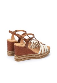 Sandalias de cuña marrones con tiras blancas, detalles de yute trenzado y plantilla acolchada. Correa de tobillo ajustable para un ajuste seguro.