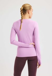 Maglietta sportiva a maniche lunghe di colore lilla chiaro, con un motivo testurizzato, vestibilità slim e polsini con fori per il pollice. Indossata con leggings scuri a motivi.