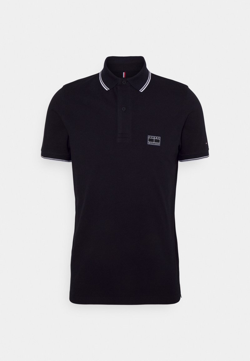 Polo noir à manches courtes avec bord blanc au col et aux manches, patte de boutonnage et petit écusson logo sur la poitrine.