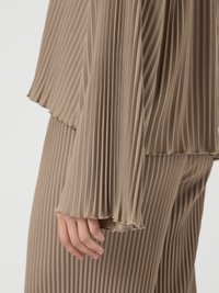 Plisseet, beige antrekk som har en langermet topp med utsvingte mansjetter, strukturert stoff og myke kanter, komplementert av matchende bukser.